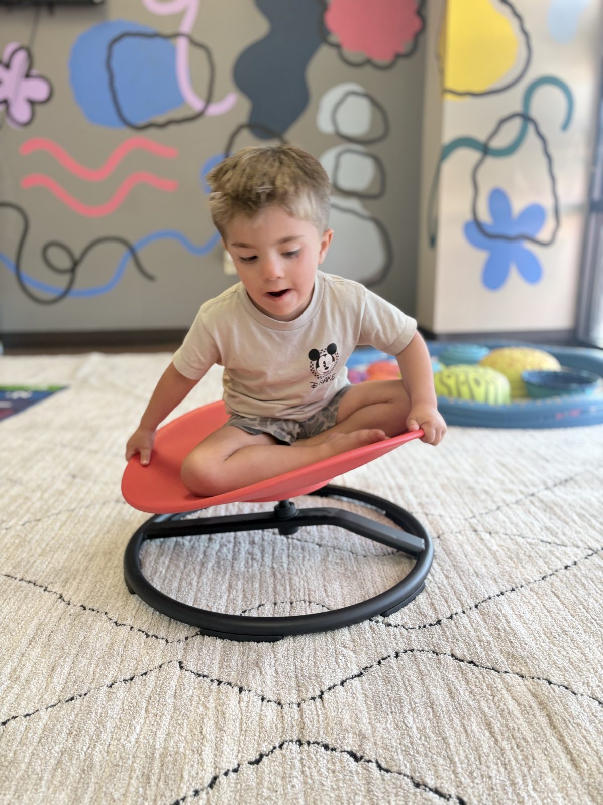 A young boy playing on a sensory spinner in our colorful clinic playroom