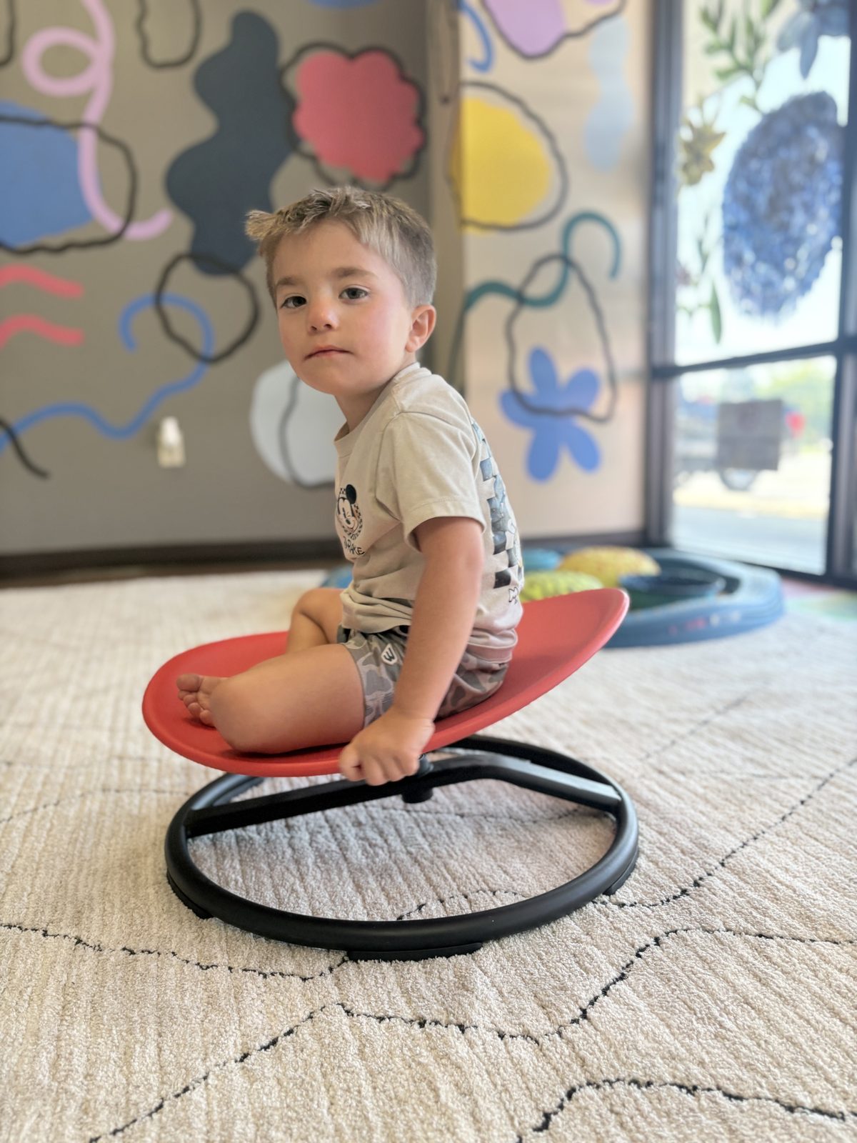 A young boy playing on a sensory spinner in our colorful clinic playroom